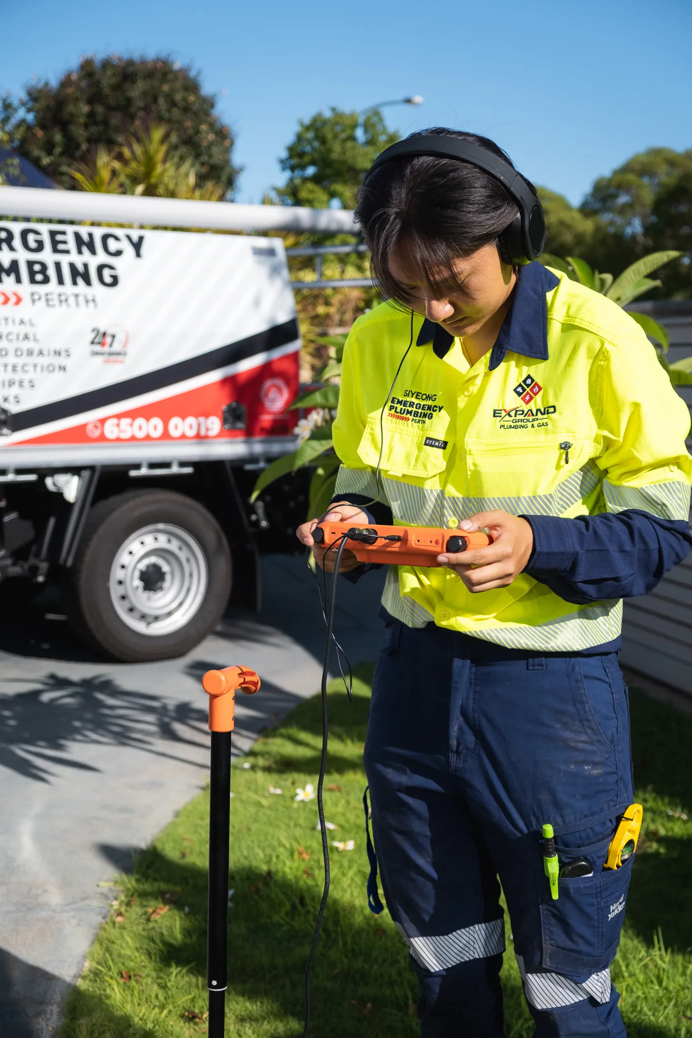 Person in a high-visibility uniform using a portable device outdoors near a utility truck.